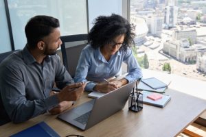A woman takes notes while a man next to her uses a computer